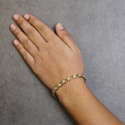 Yellow bracelet with heart-shaped links set with multiple white round gemstones in prong settings, shown worn on a model’s wrist from a top front angle.
