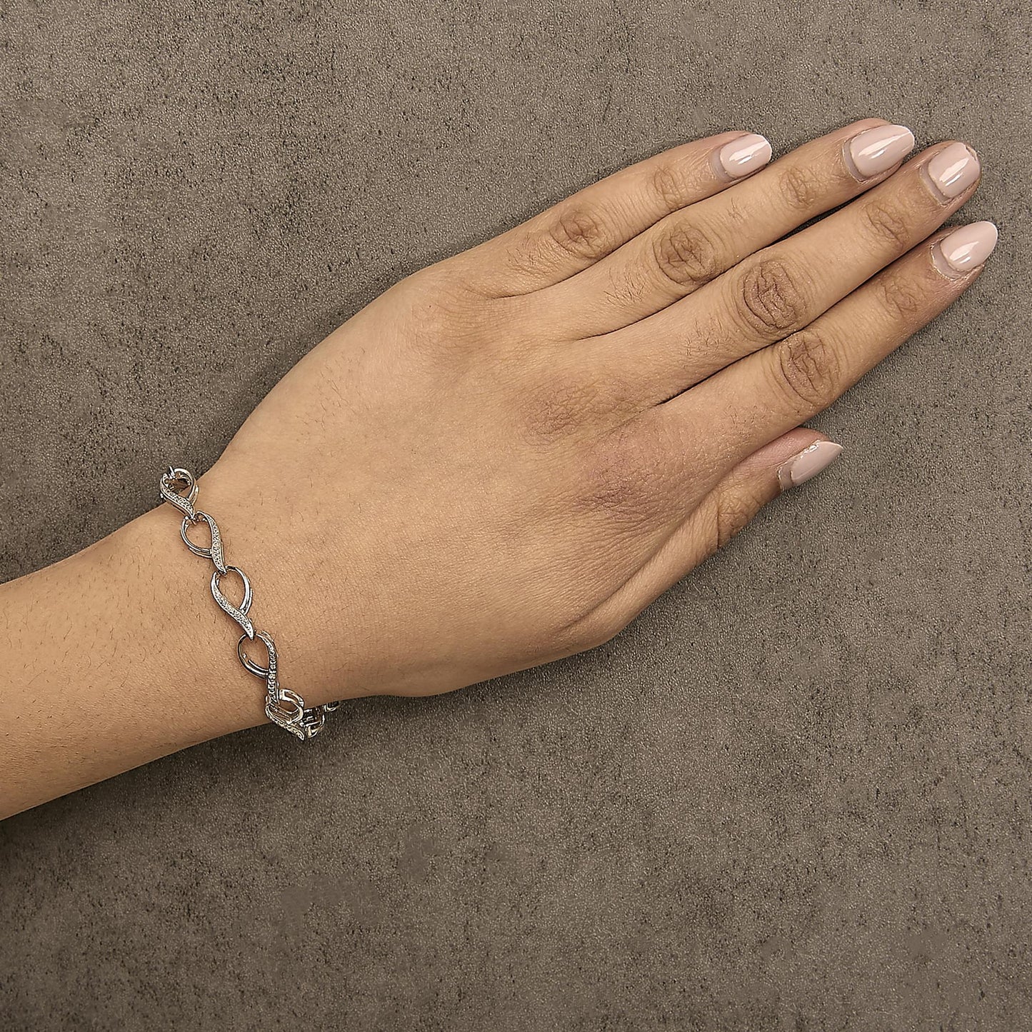 Bracelet with alternating polished links and links paved with small white gemstones in prong settings, shown worn on a model's wrist from a top-down angle.