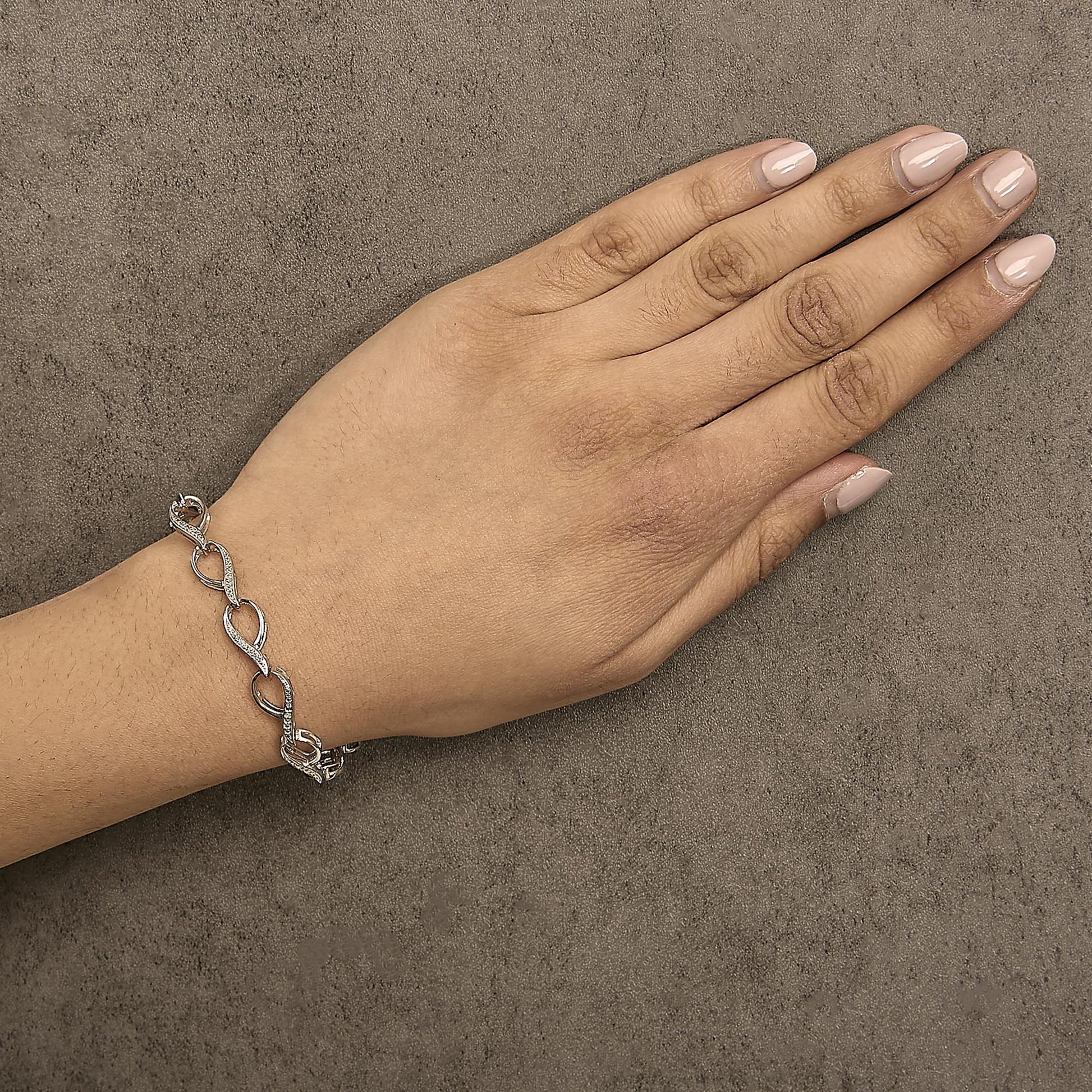 Bracelet with alternating polished links and links paved with small white gemstones in prong settings, shown worn on a model's wrist from a top-down angle.