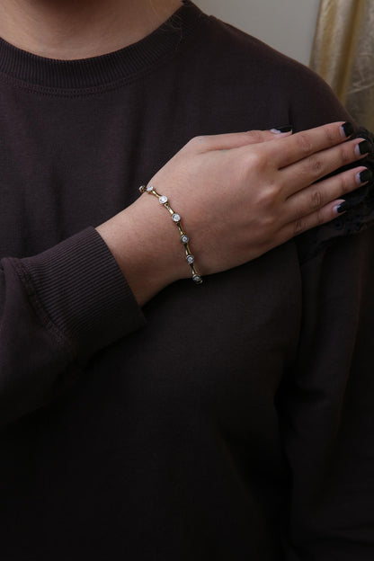 Yellow metal bracelet with round white gemstones in miracle settings, shown on a model's wrist from a front angle.