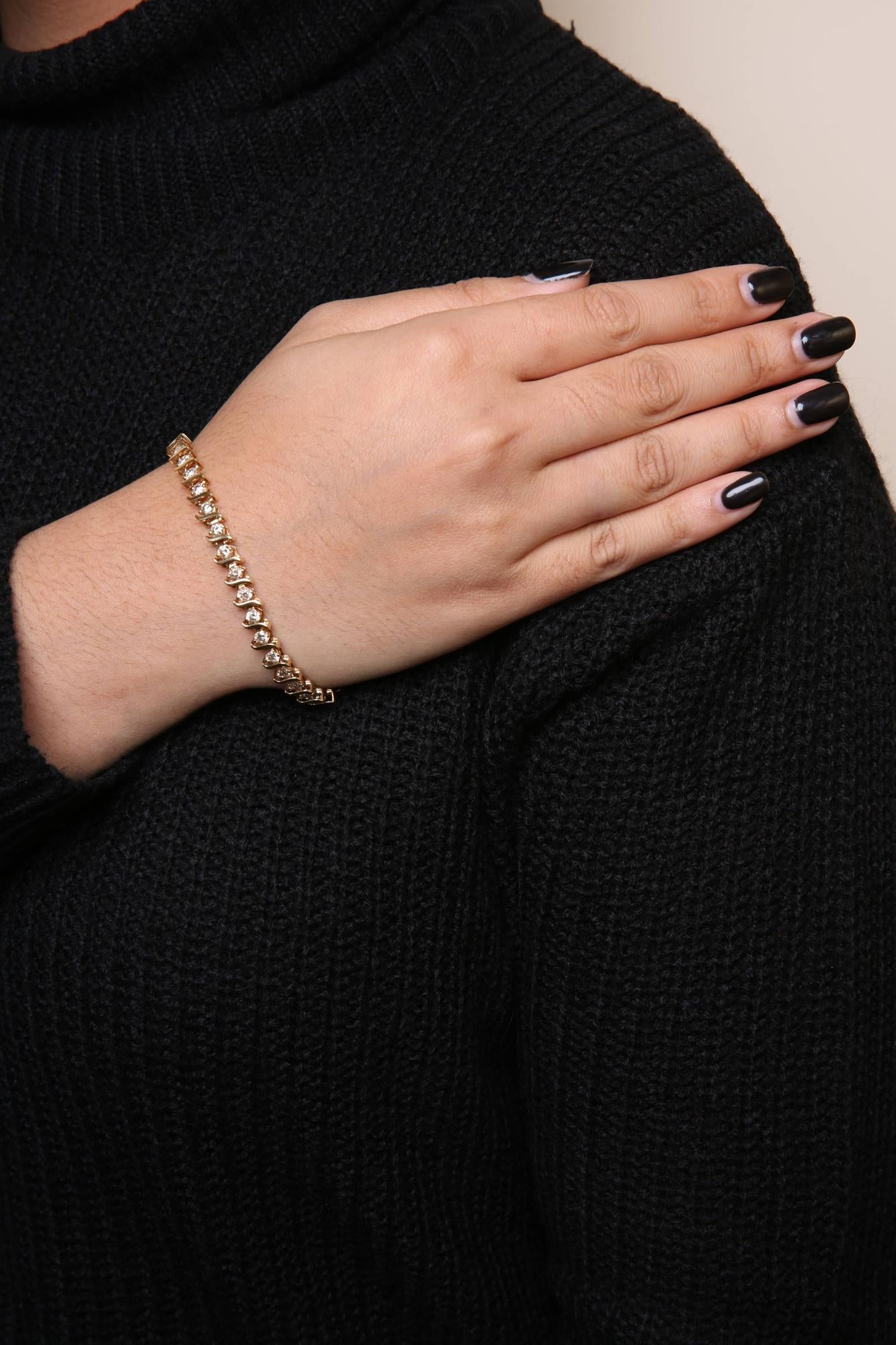 Yellow metal bracelet with brownish round gemstones in prong settings, worn on a model's wrist, shot from a side angle.