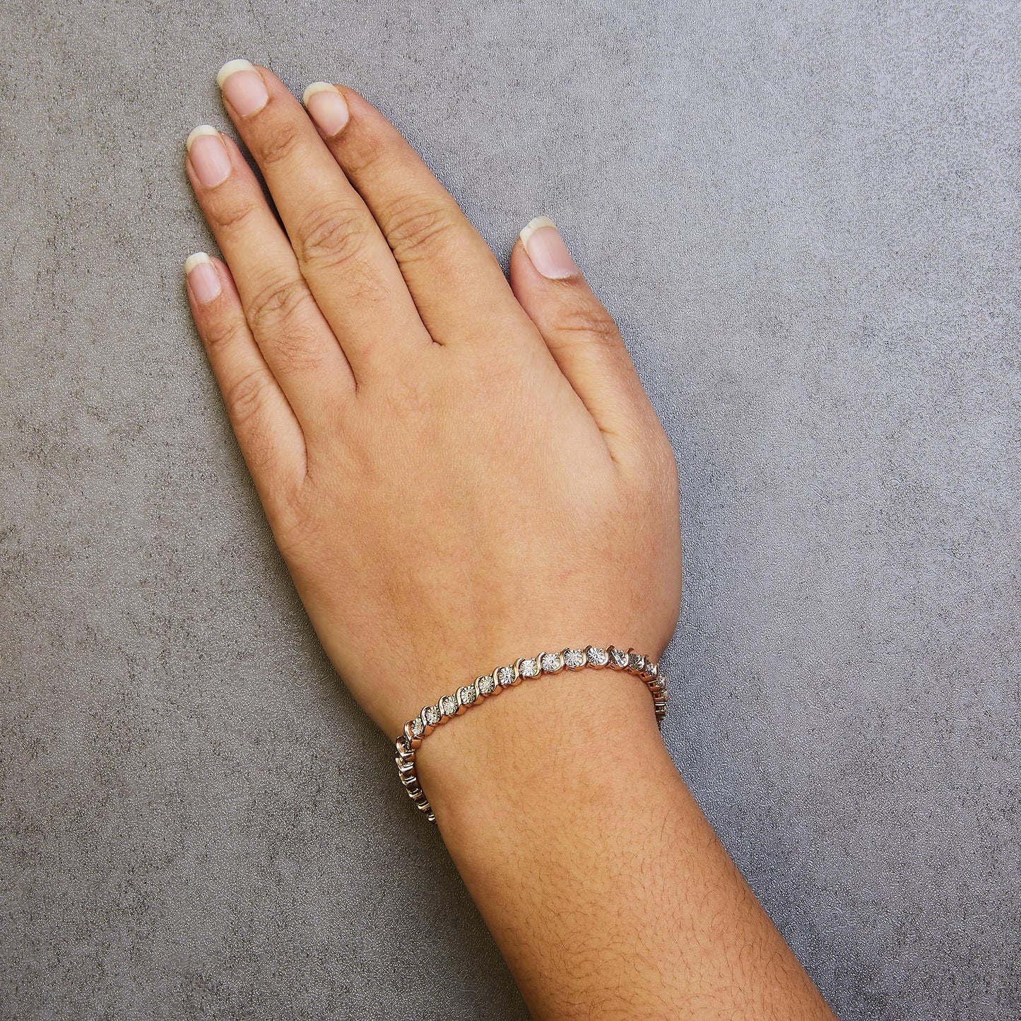 Close-up shot of a rose-colored bracelet with round white gemstones in miracle settings, worn on a model's wrist against a gray textured background.