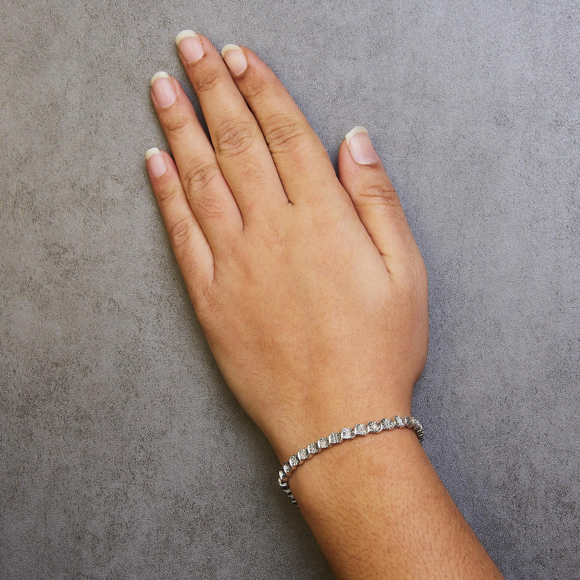 White metal bracelet with round white gemstones in miracle setting, worn on wrist, top angle view.