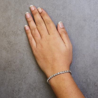 White metal bracelet with round white gemstones in miracle setting, worn on wrist, top angle view.
