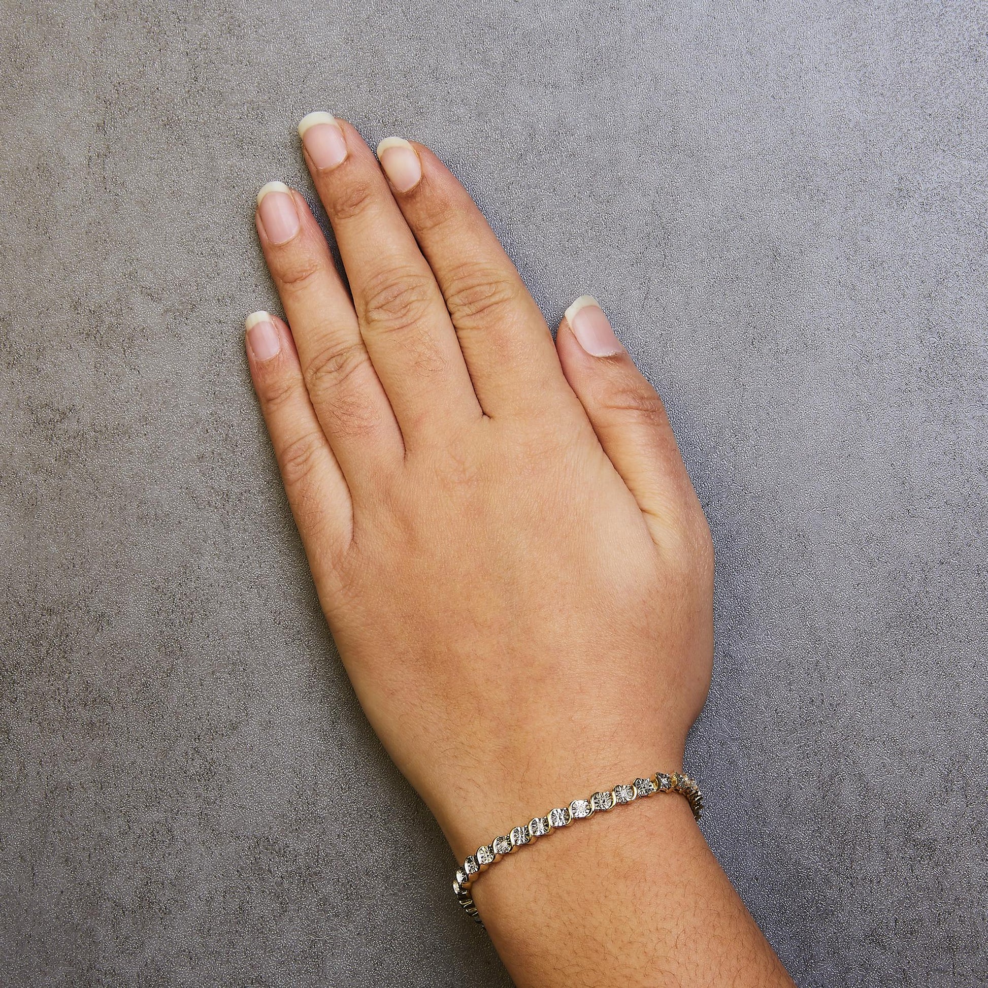 Yellow bracelet with round white gemstones in miracle setting on wrist, top-down angle.