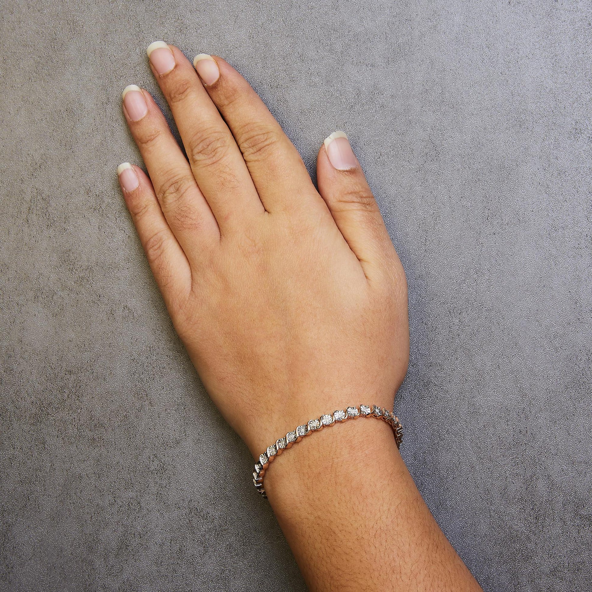 Rose-colored bracelet with round white gemstones in miracle setting on a model's wrist, top-down angle.