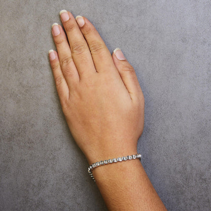 Close-up top view of a white metal bracelet with round white gemstones in a miracle setting, worn on a model's wrist.