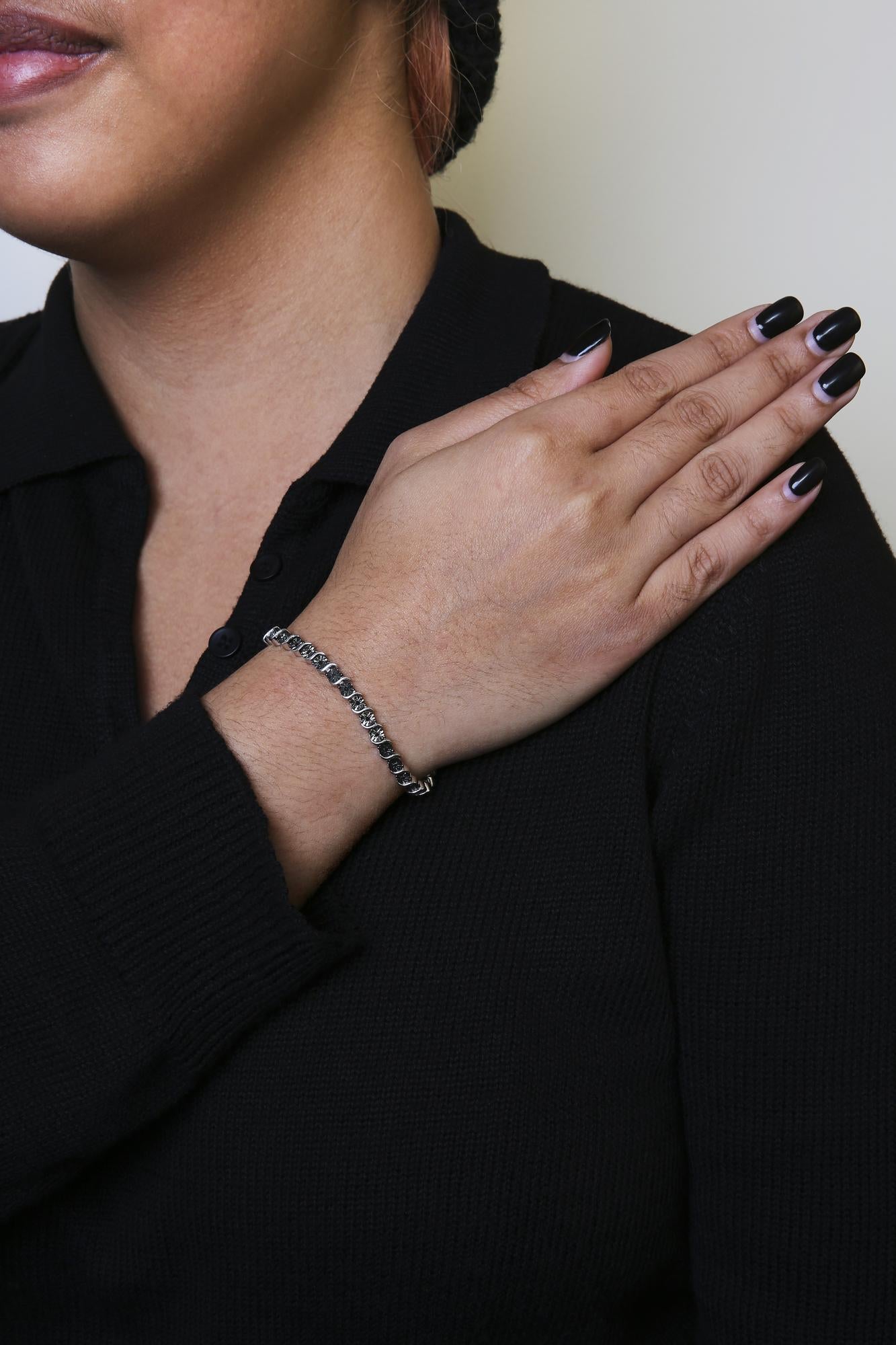 White metal bracelet with round black gemstones in miracle settings, worn on a model's wrist, shot from a side angle.