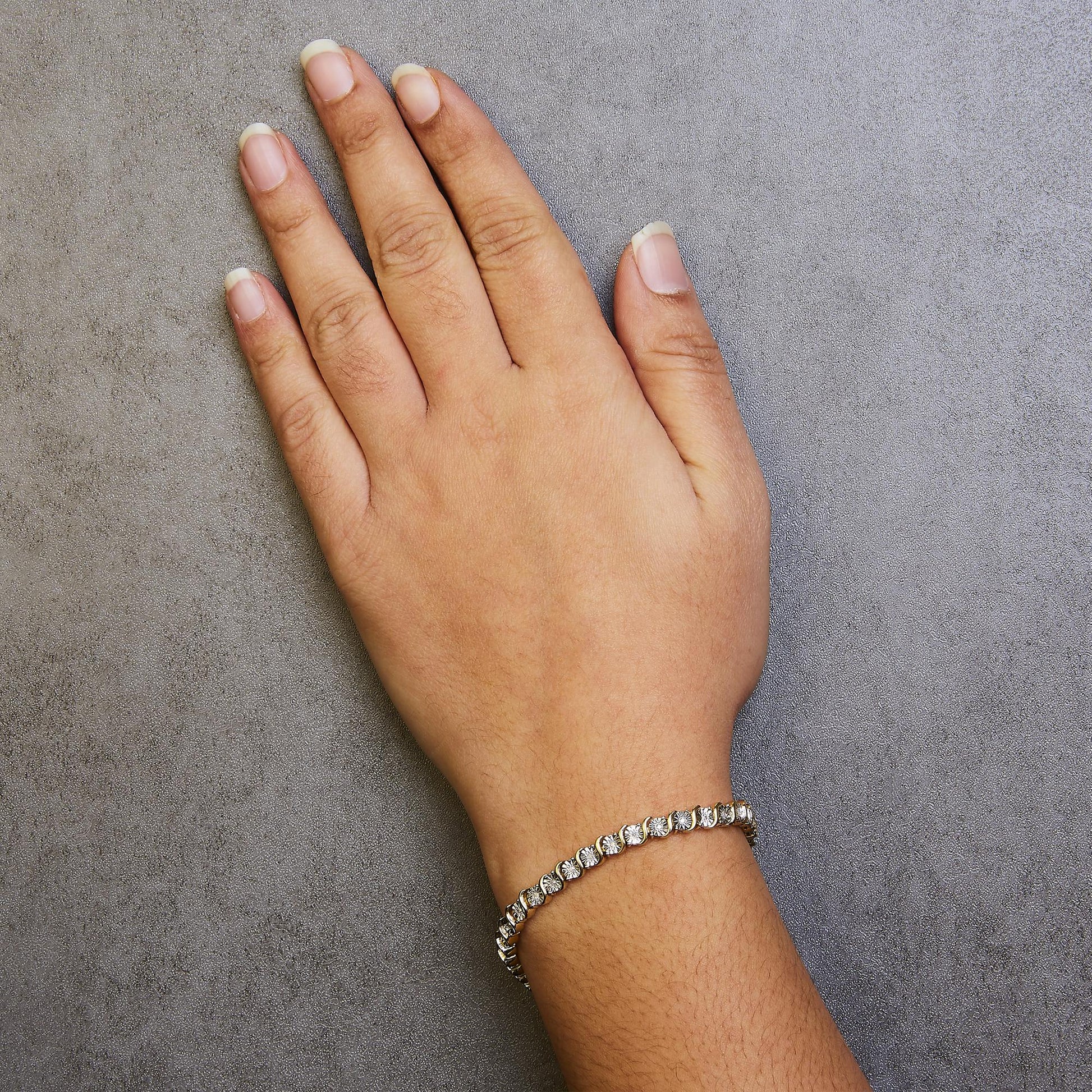 Yellow metal bracelet with round white gemstones in miracle setting worn on wrist, top-down view.