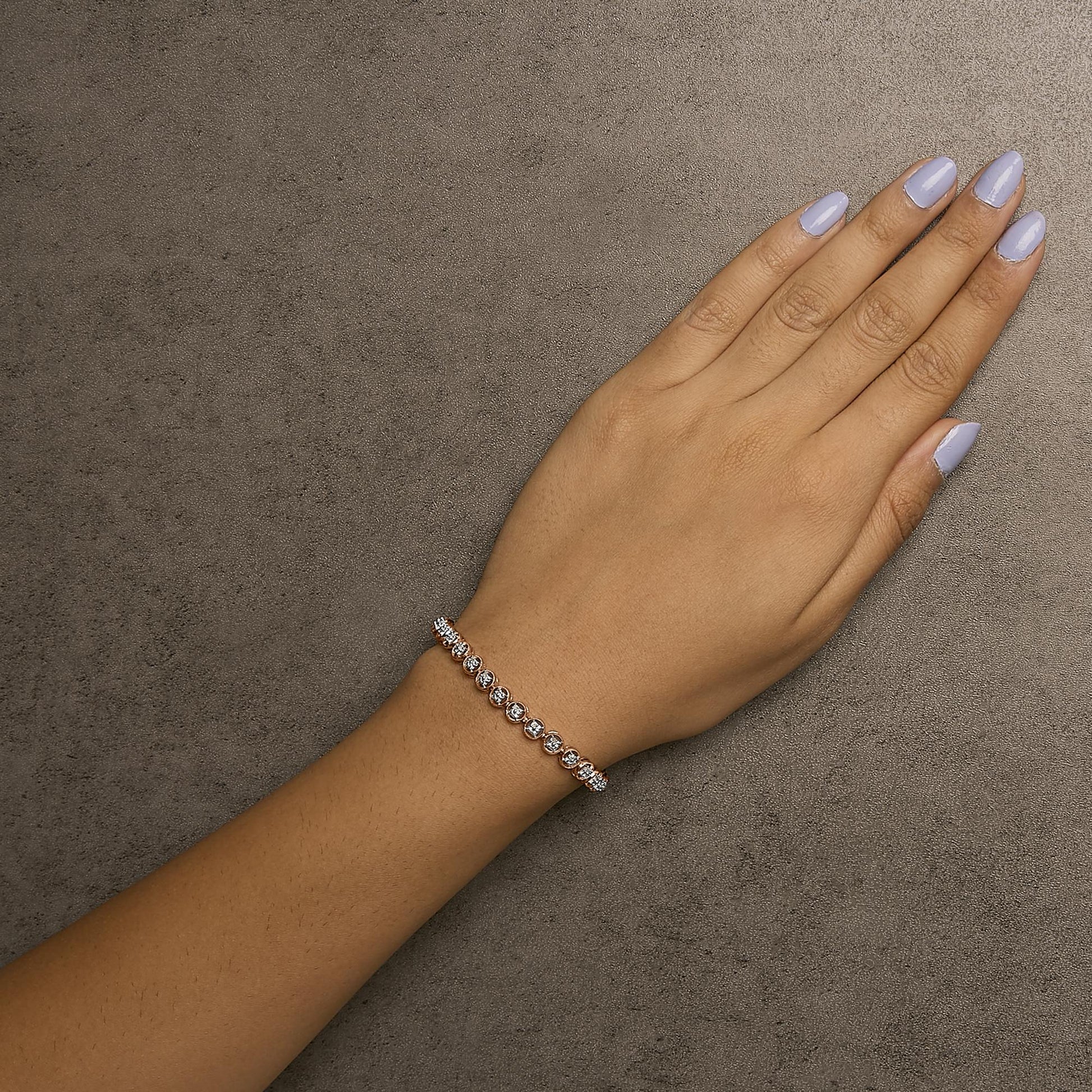 Rose metal bracelet with prong-set round white gemstones, worn on wrist, top-down angle.