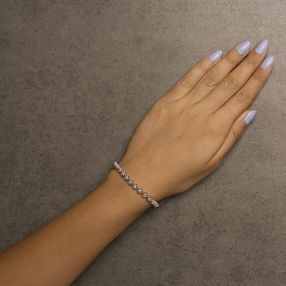 Rose metal bracelet with prong-set round white gemstones, worn on wrist, top-down angle.