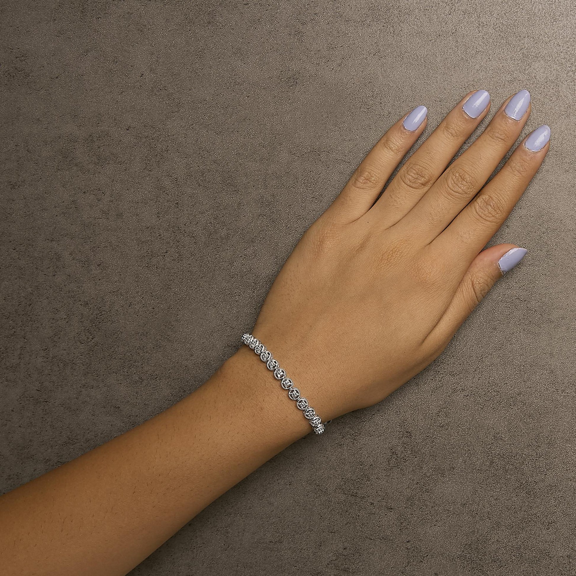 Bracelet with round white gemstones in prong setting displayed on a model's wrist, shot from above.