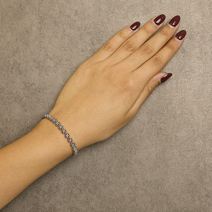 Rose metal bracelet with round white gemstones in prong settings, shown on wrist from above angle.