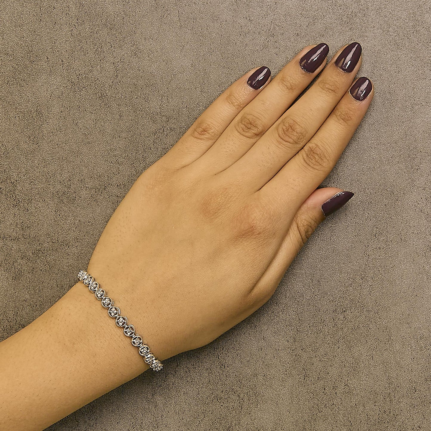 White metal bracelet with round white gemstones in prong settings, shown on a model's wrist from a top-down angle.