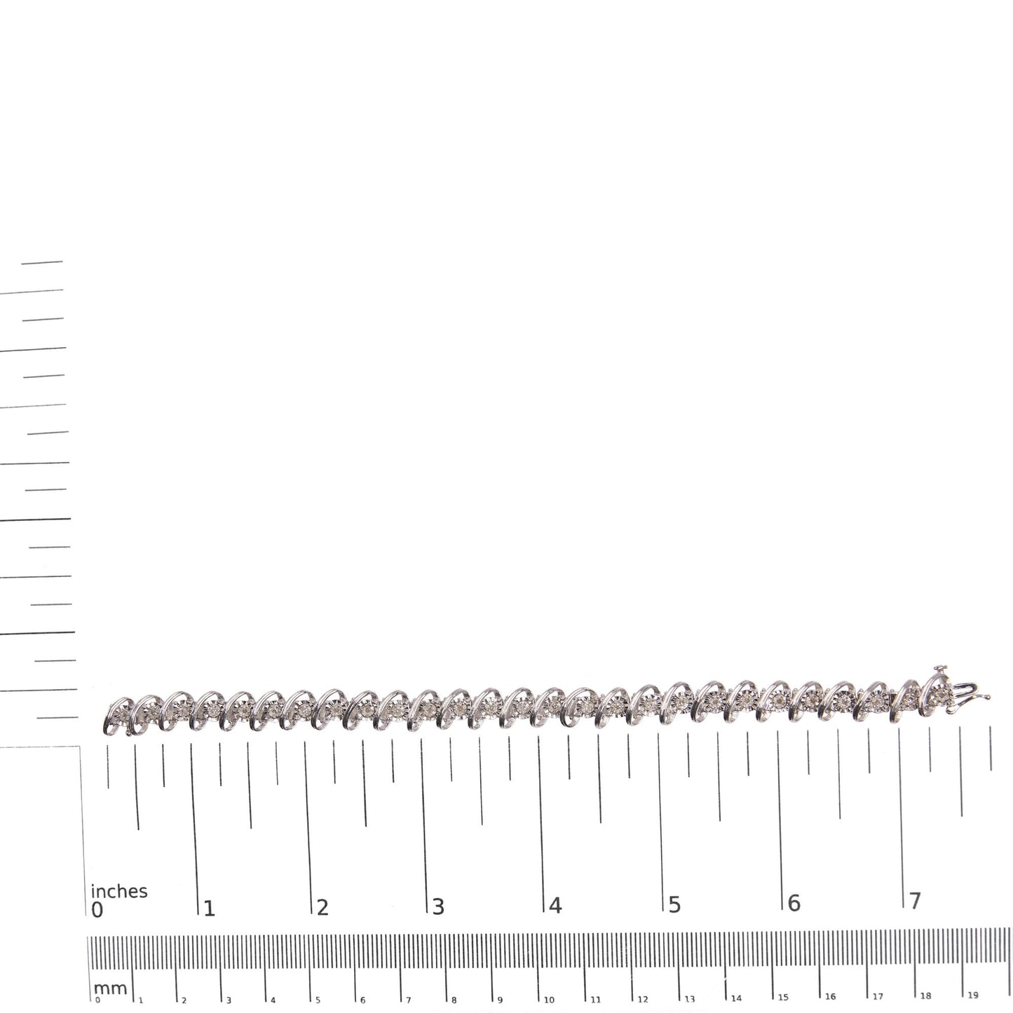 White bracelet with round white gemstones in miracle and prong settings, placed horizontally on a ruler and scale for size reference, photographed from above.