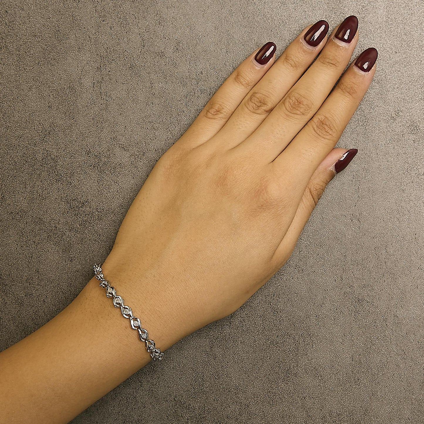 White metal bracelet with round white gemstones in miracle settings, shown on a model's wrist from a top angle.