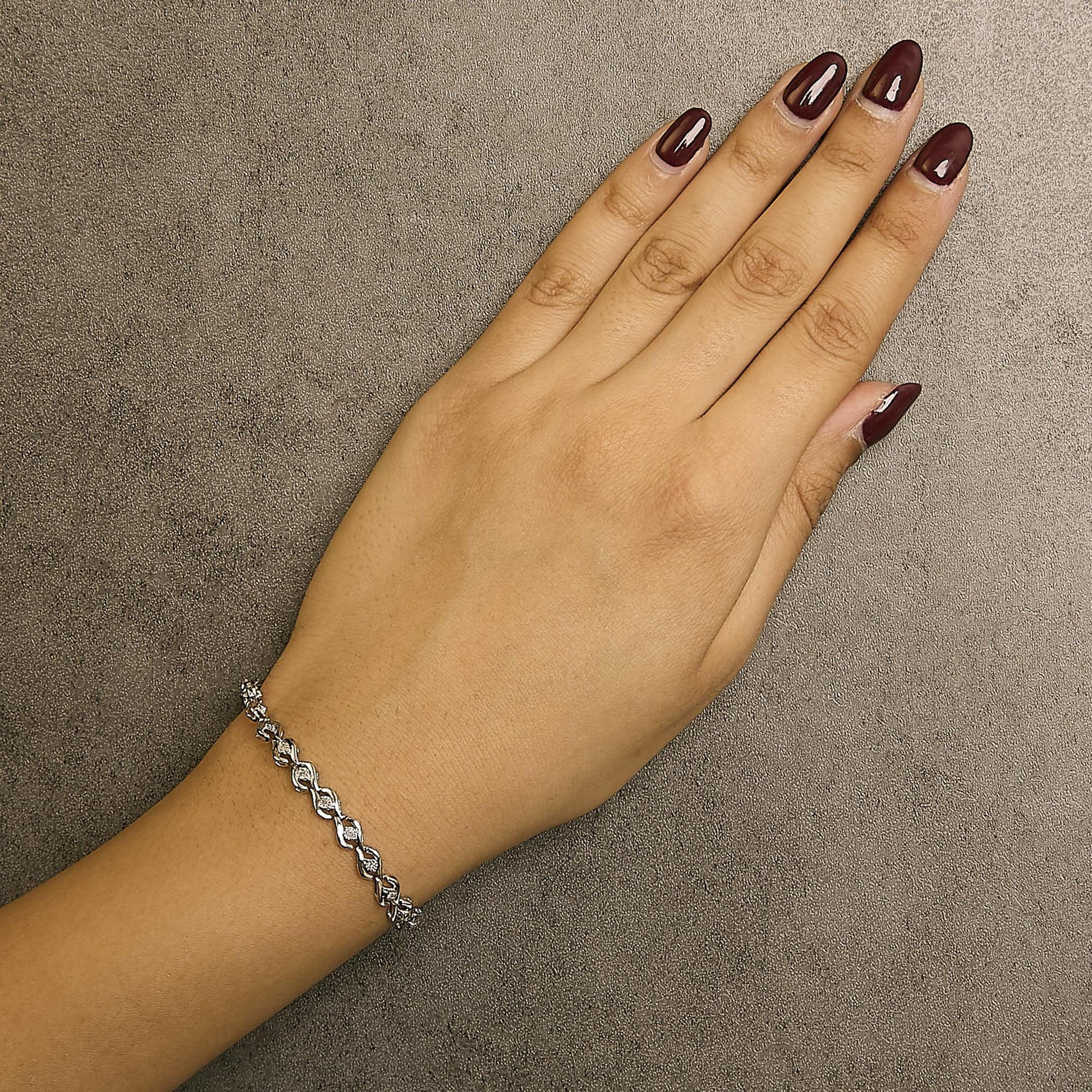 White metal bracelet with round white gemstones in miracle settings, shown on a model's wrist from a top angle.