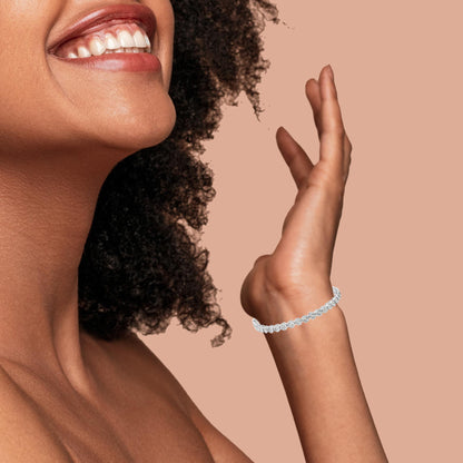 Close-up side view of a smiling model wearing a white metal bracelet with round white gemstones in a miracle setting on her wrist.