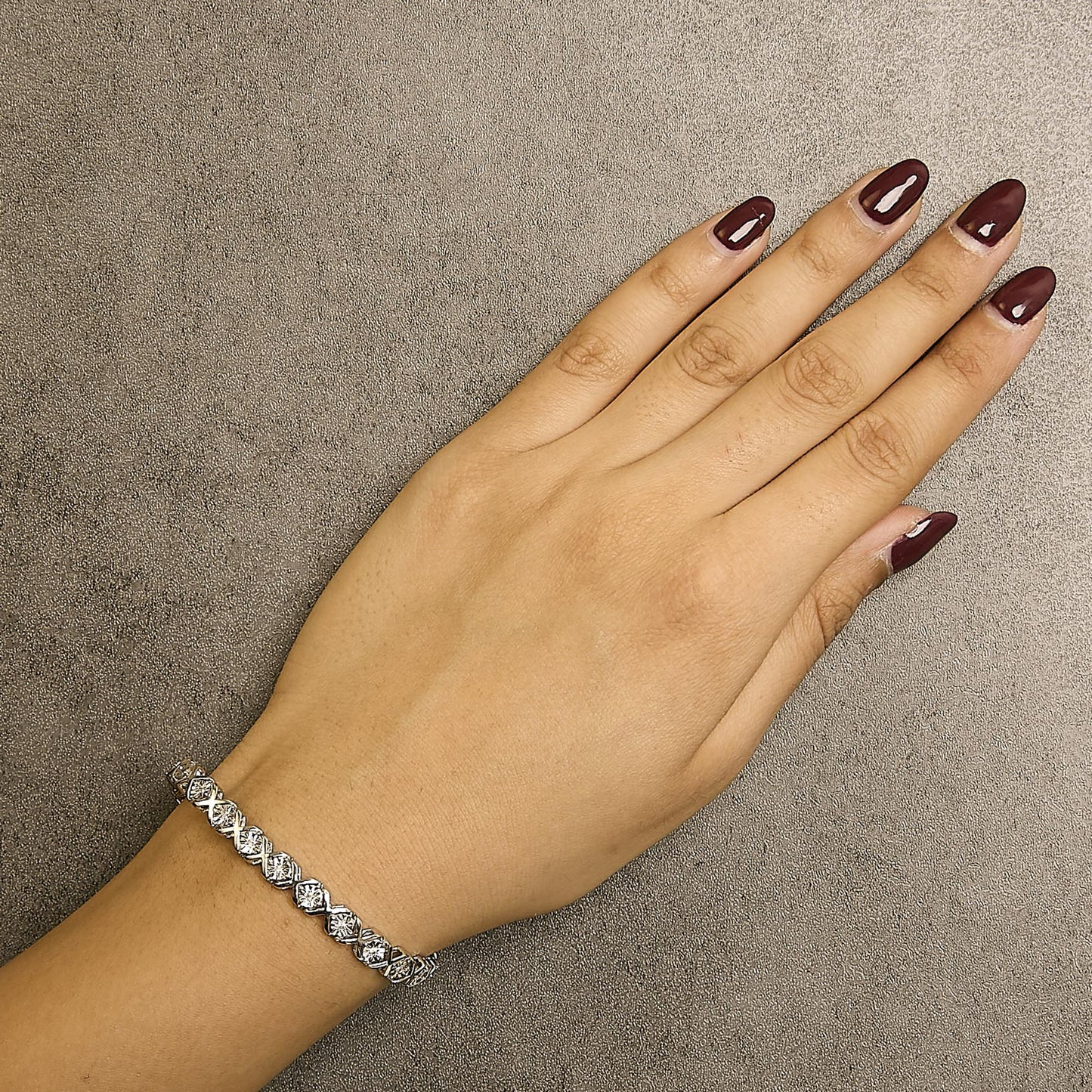 White metal bracelet with round white gemstones in miracle setting, worn on a model's wrist, top-down angle.