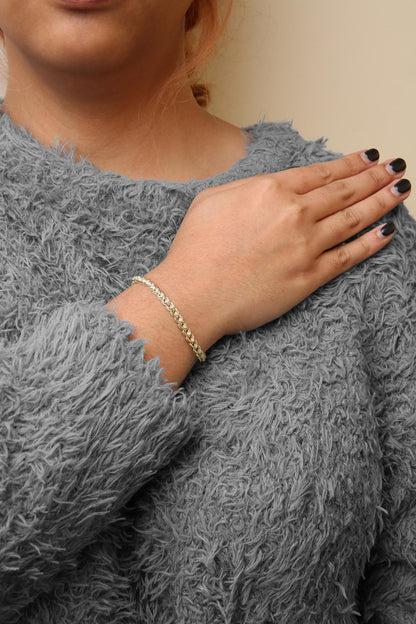 Yellow metal bracelet with round white gemstones in prong setting, worn on a model's wrist, shot from the front angle.