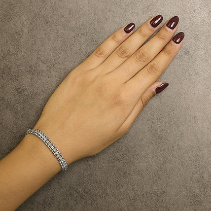 White metal bracelet with round white gemstones in prong settings, worn on wrist, top-down angle.