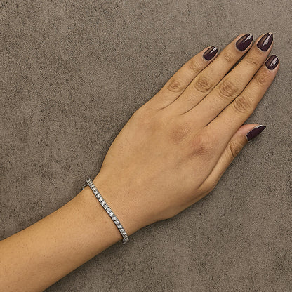 White metal bracelet with round white gemstones in a miracle setting, worn on a model's wrist, shown from a top-down angle.