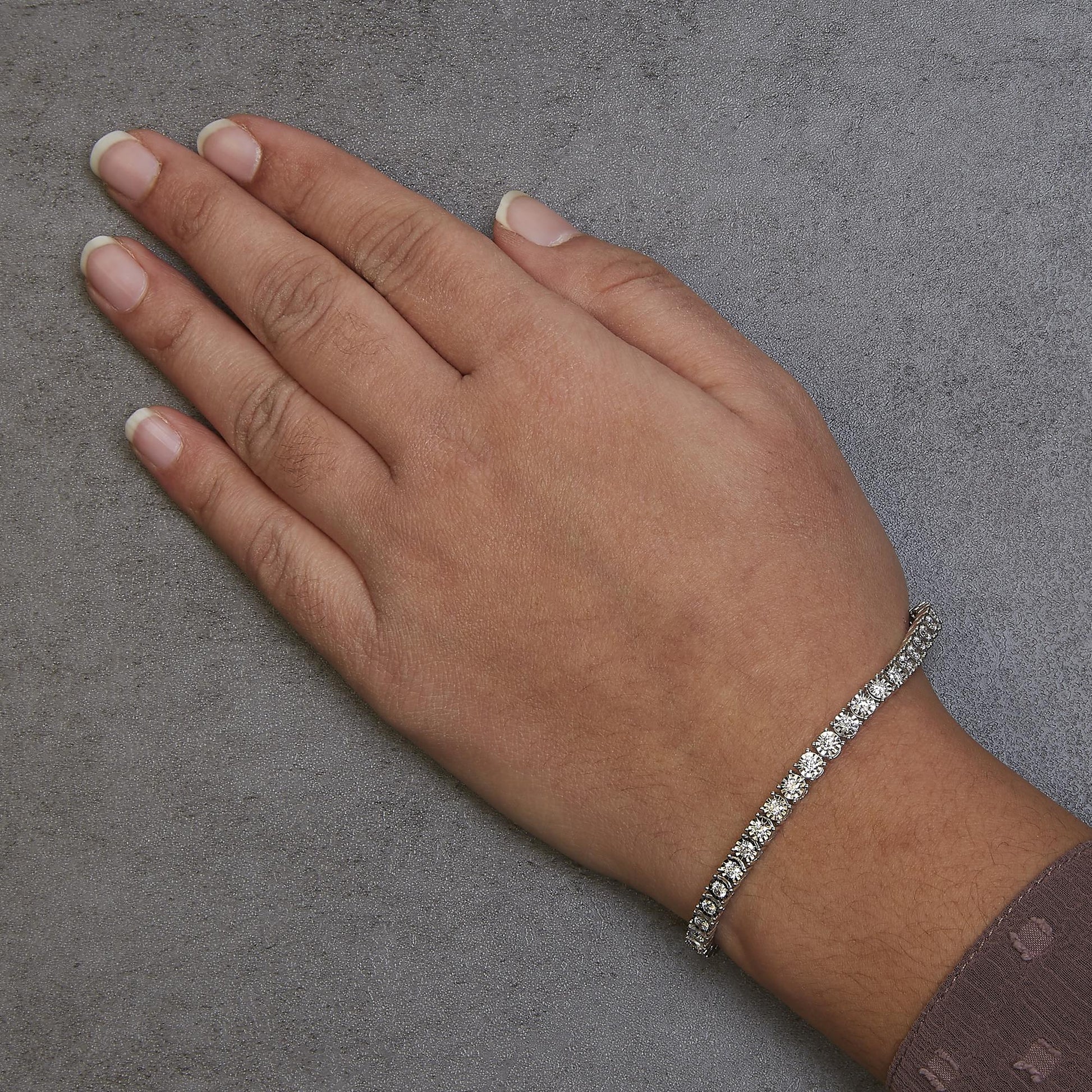 White metal bracelet with round white gemstones, worn on a model's wrist, shot from above at an angle.