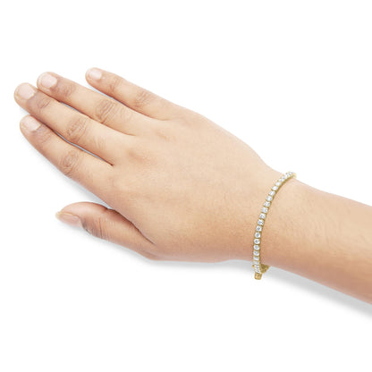 Yellow metal bracelet with white round gemstones in 4-prong settings, shown on a model's wrist, angled top-down.