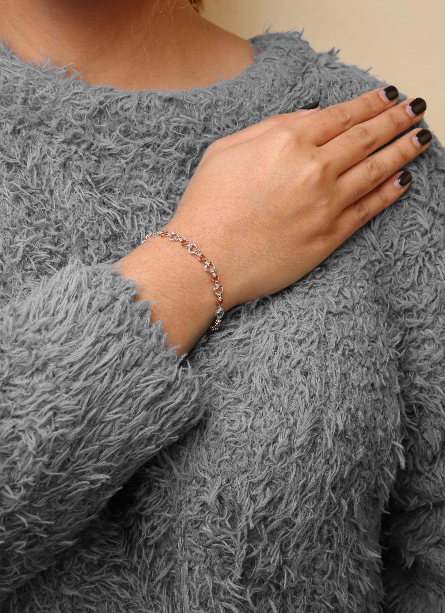 Bracelet with alternating white and rose colored heart-shaped links adorned with round white gemstones, worn on a model's wrist, front side view.