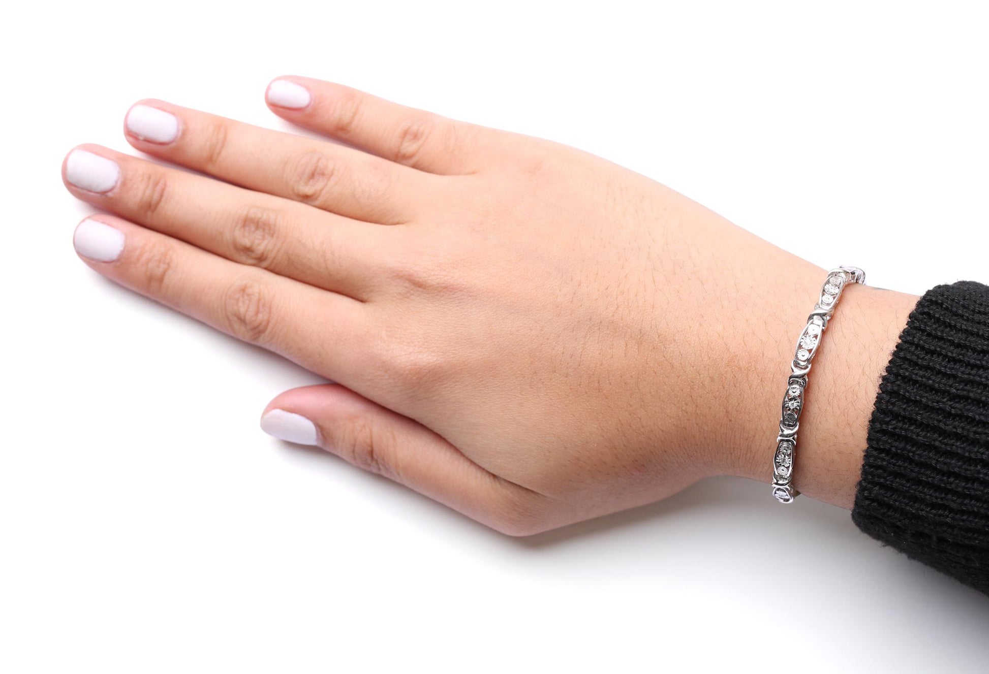 White metal bracelet with round white gemstones in miracle settings, worn on a model's wrist, top-down angle.