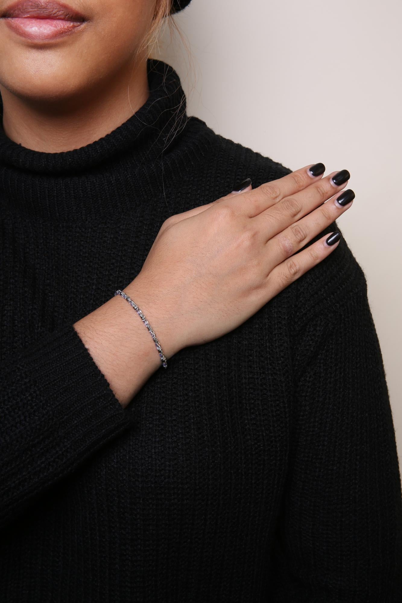 Close-up front-angle shot of a white bracelet on a model's wrist, featuring alternating prong-set round black gemstones and marquise-shaped blue gemstones.