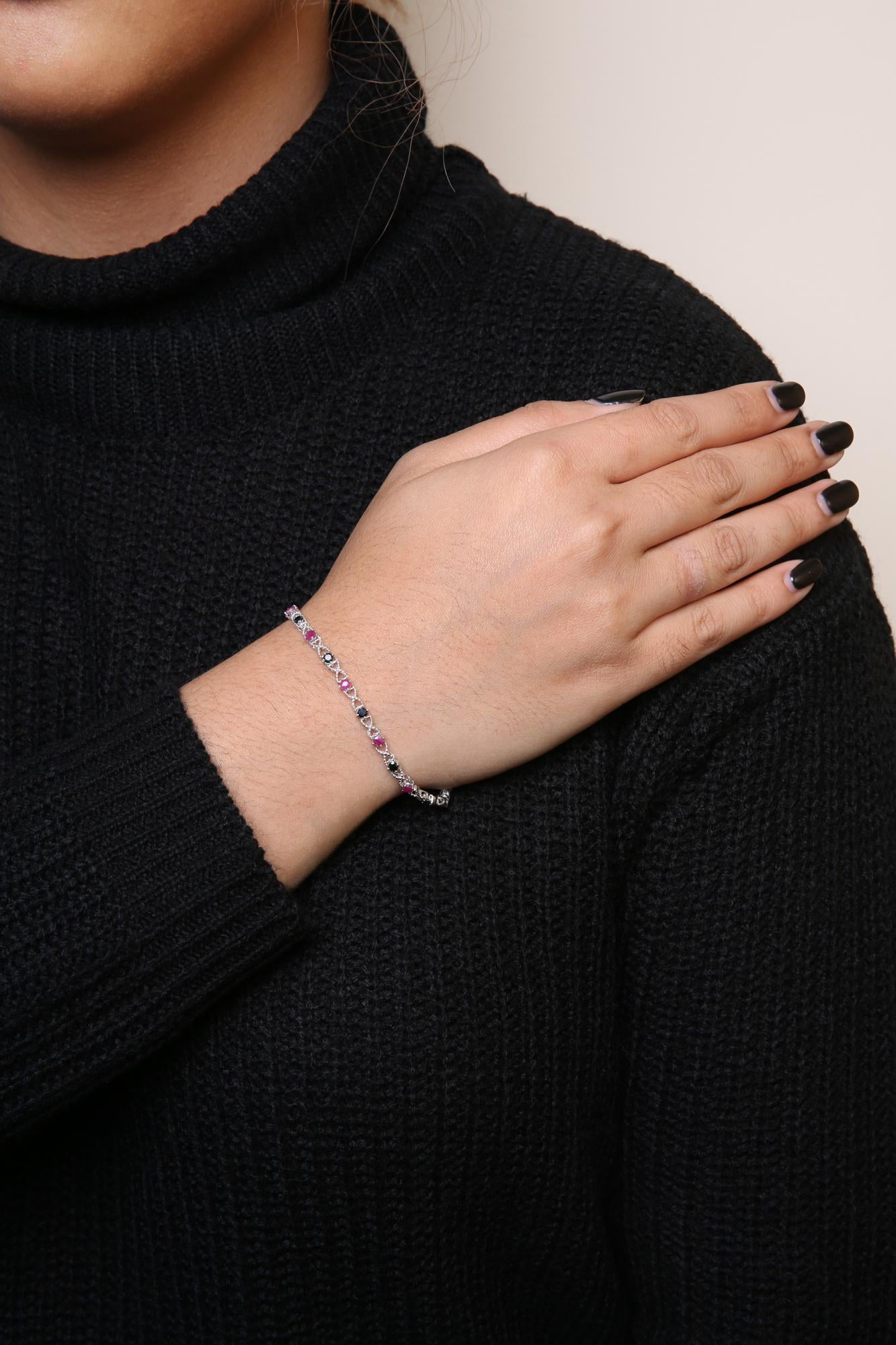 White metal bracelet with alternating round pink and black gemstones in prong settings, worn on model's wrist, shown in close-up angled view.