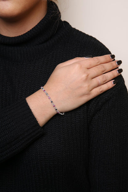 White metal bracelet with alternating round pink and black gemstones in prong settings, worn on model's wrist, shown in close-up angled view.