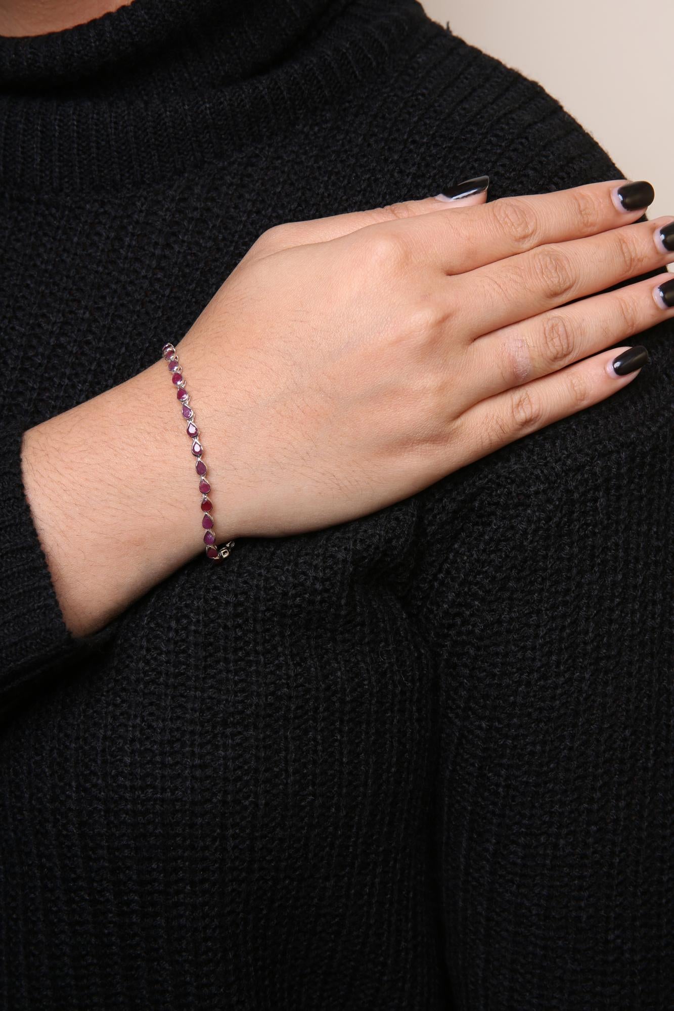 Close-up side angle of white metal bracelet with red gemstones on a model's wrist against a black textured sweater background.