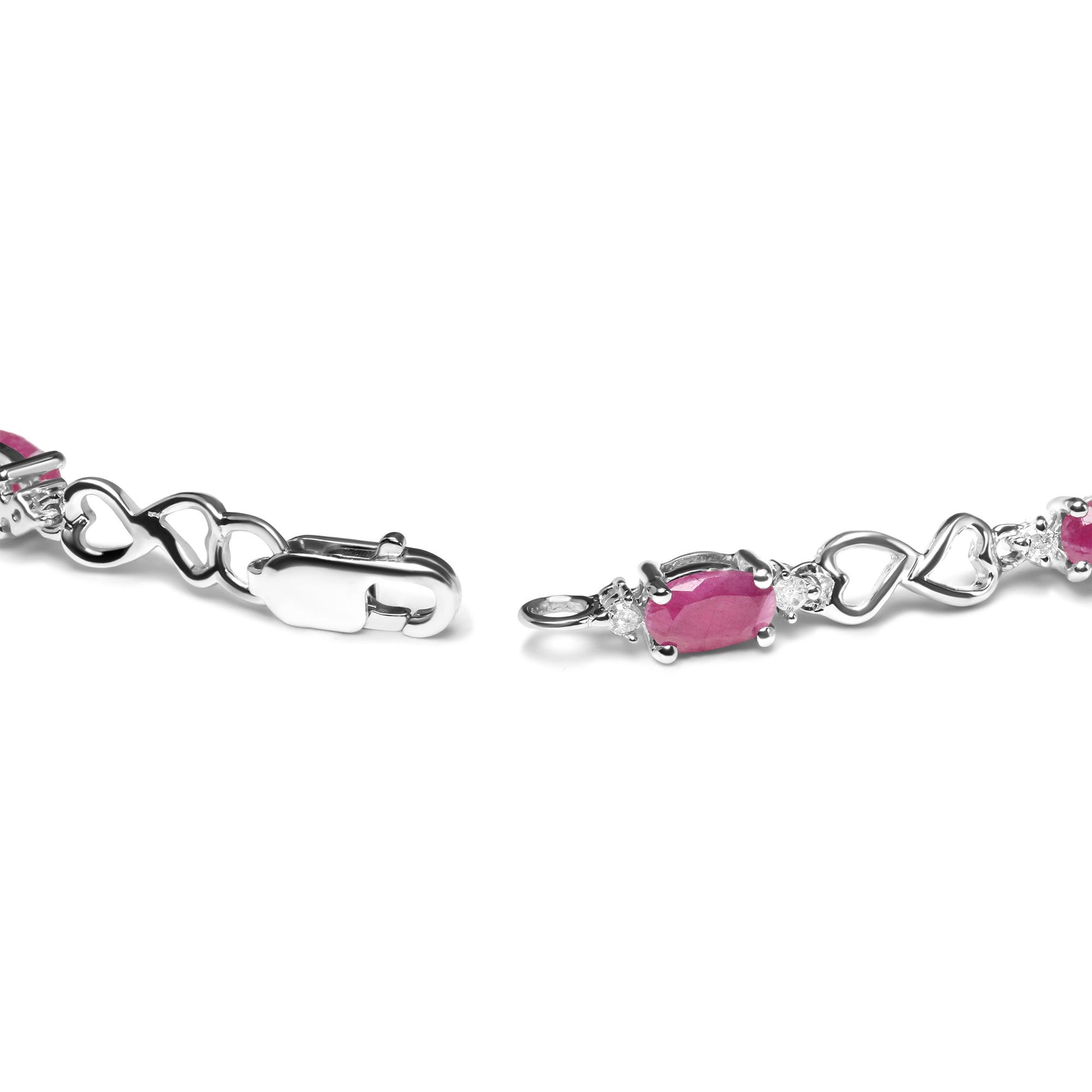 Close-up side angle of a white metal bracelet featuring oval pink gemstones in prong settings, alternating with heart-shaped links and round white gemstones in prong settings, showing the clasp end.