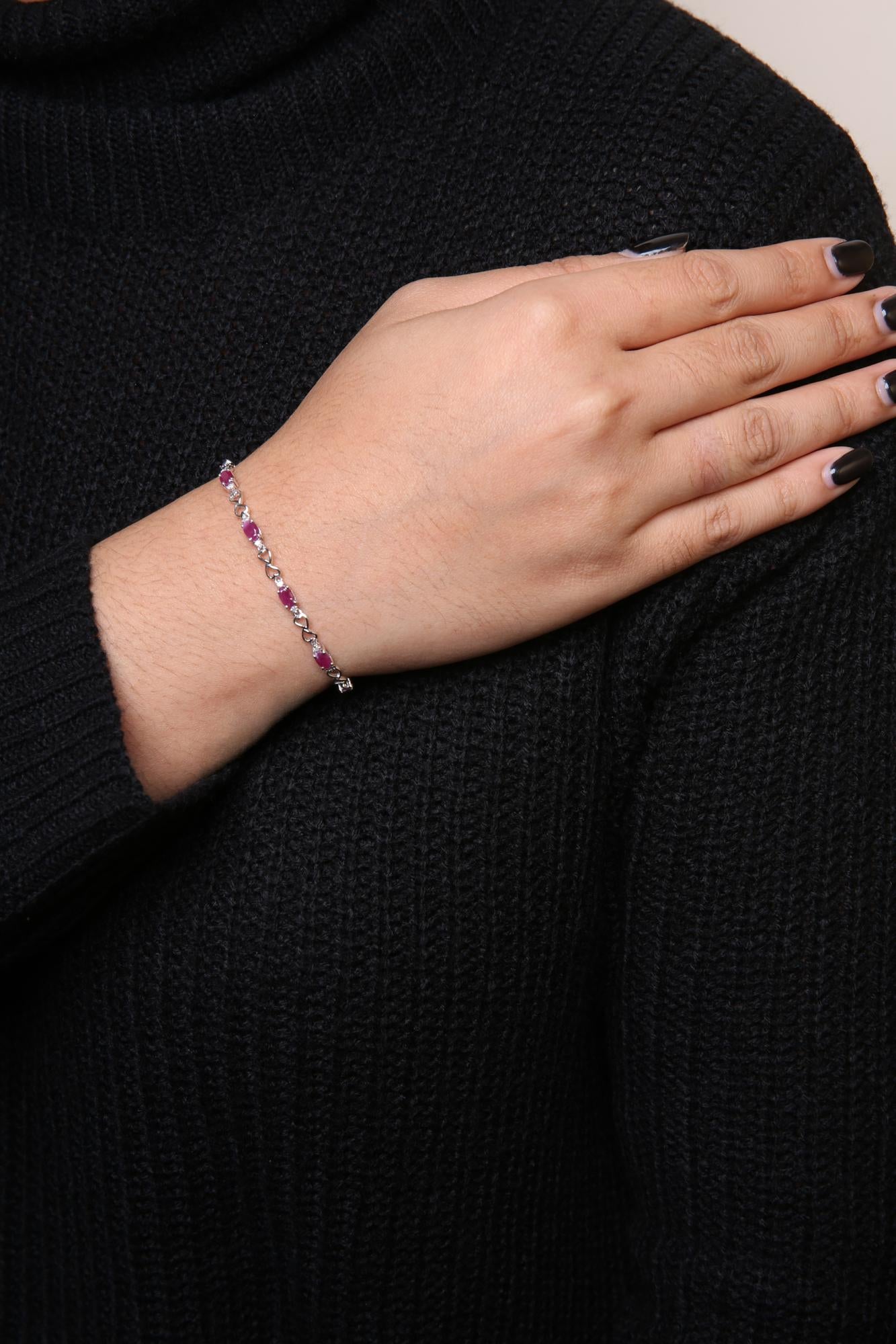 White metal bracelet with alternating oval pink gemstones and round white gemstones in prong settings, shown on a model's wrist from a side angle.