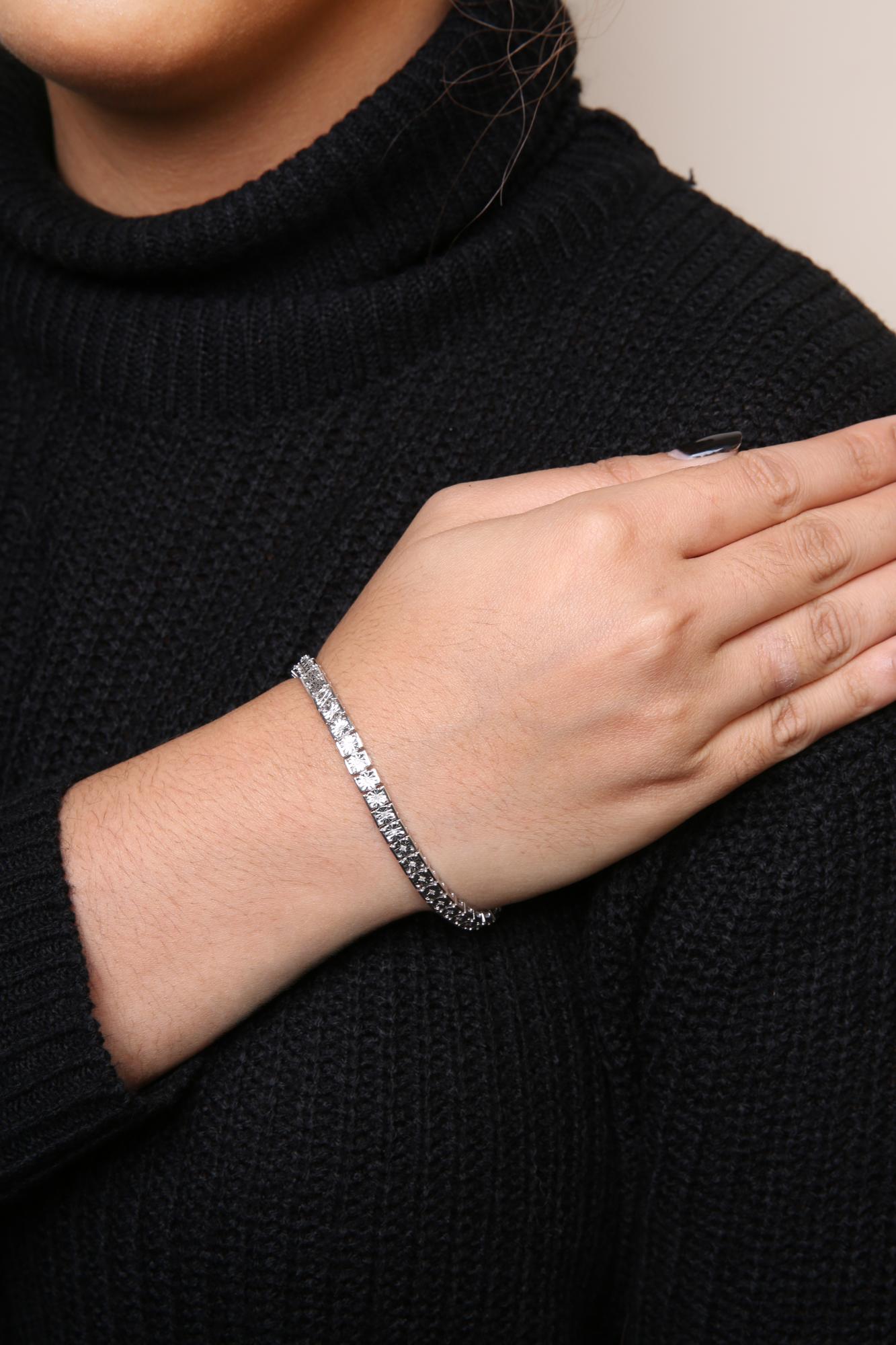 Close-up angled shot of a wrist on a model wearing a white metal bracelet featuring round white gemstones in a miracle setting.