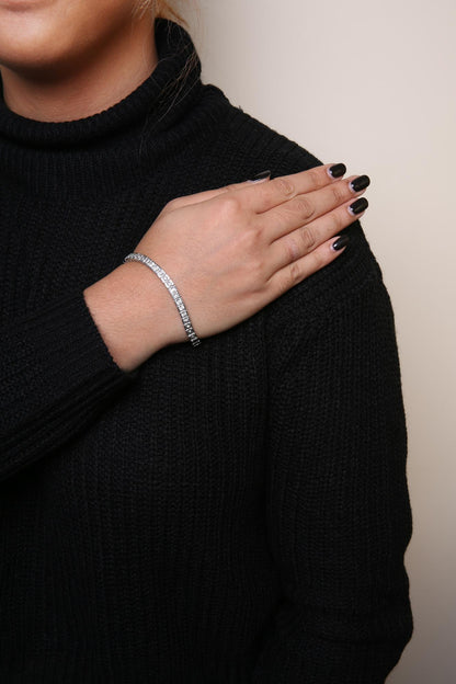 White metal bracelet with round white gemstones in miracle setting, worn on wrist of a model, front angle.