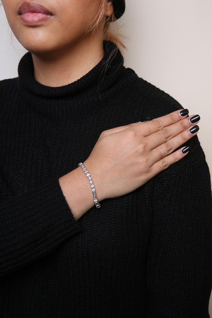 Close-up of a white metal bracelet with round white gemstones in a miracle setting, worn on a model's wrist, shot from the side angle.