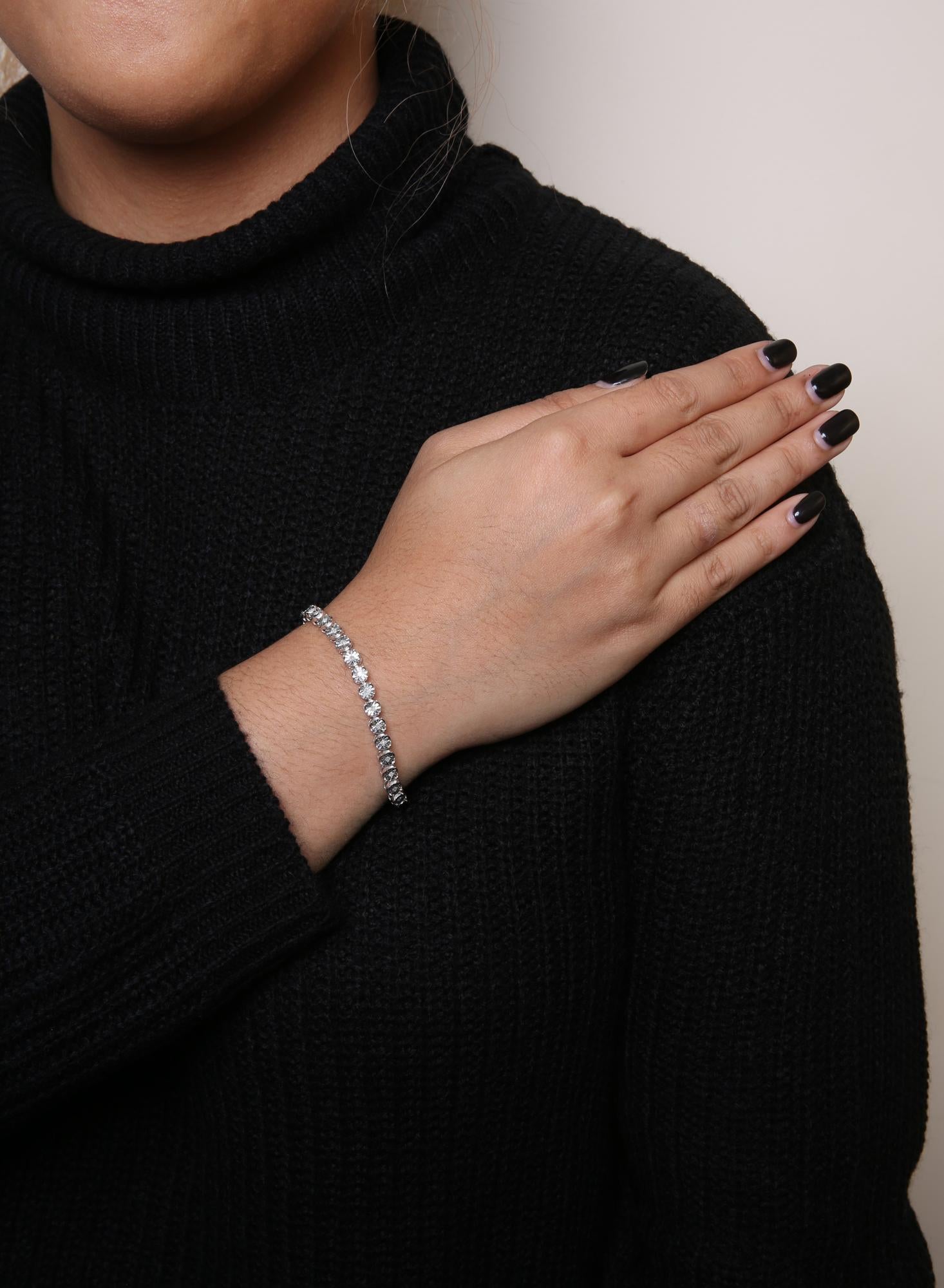 White metal bracelet with round white gemstones in miracle setting, worn on a model's wrist, shot from a front angle.
