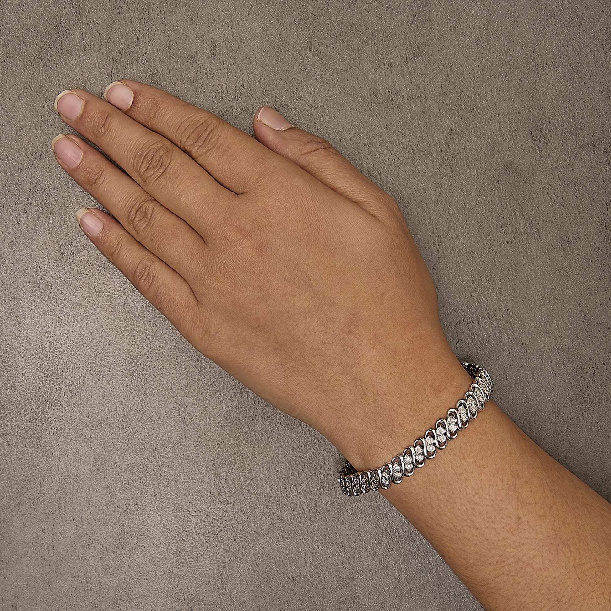 White metal bracelet with round white gemstones in miracle setting, worn on a model's wrist, top-down angle.