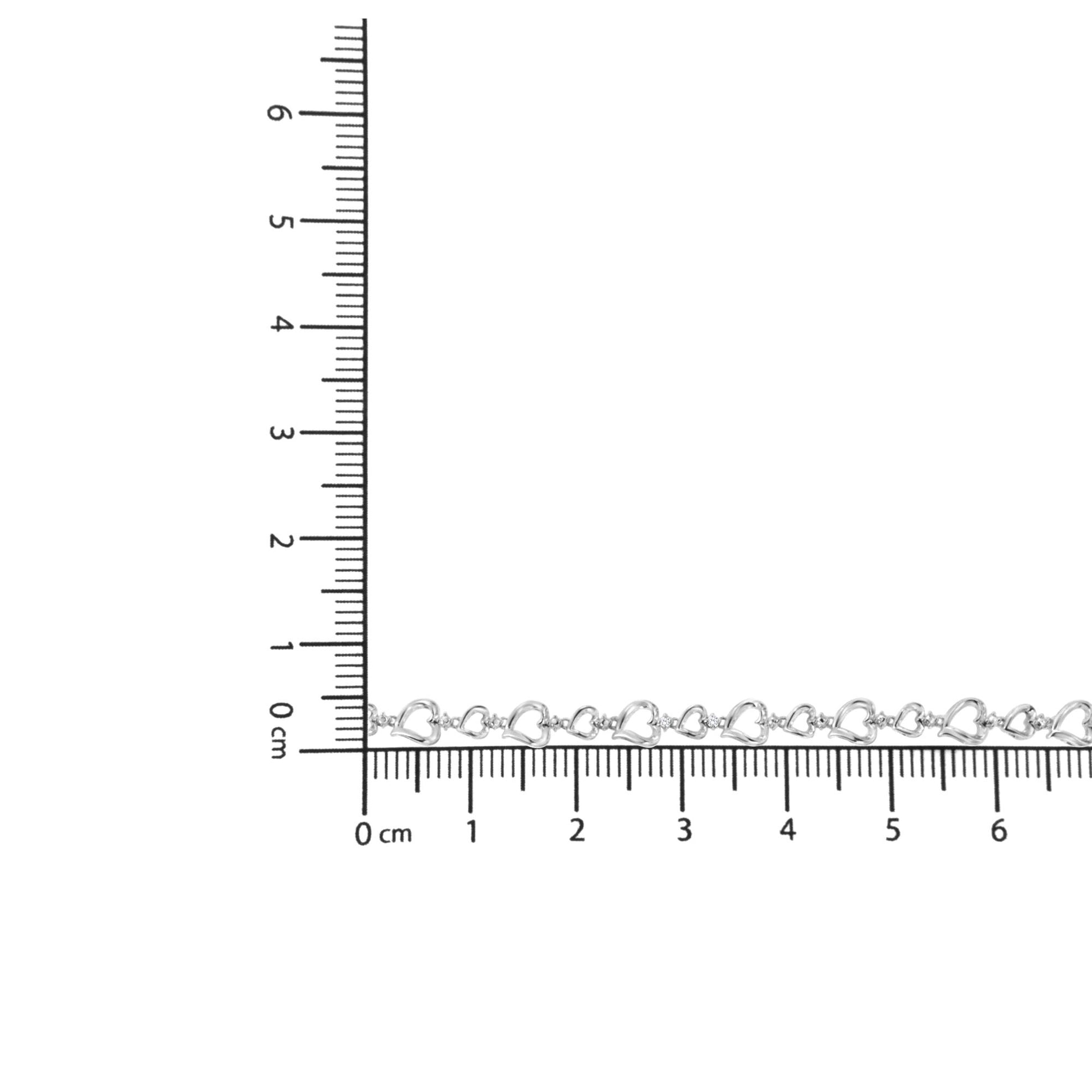 White metal bracelet with small open heart links and two round white gemstones, shown on a ruler for size reference, shot from above.