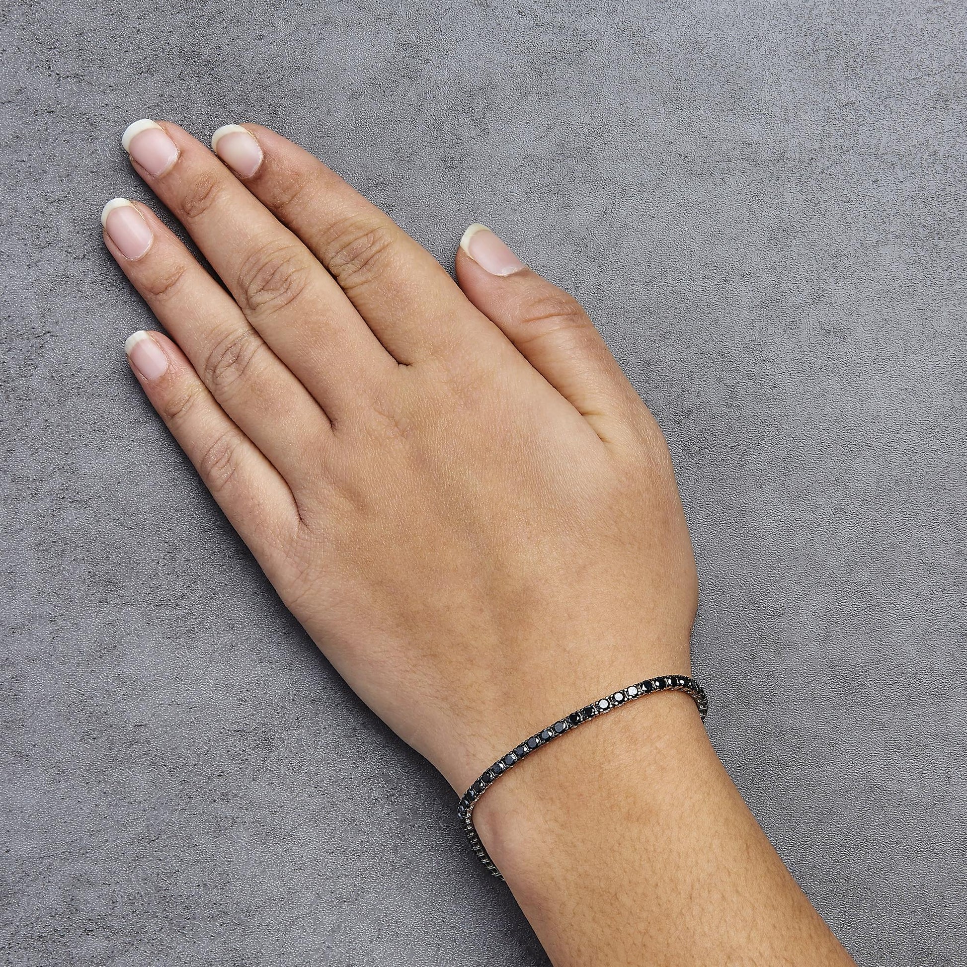 White metal bracelet with alternating black and white round prong-set gemstones on a model's wrist, top-down angle.