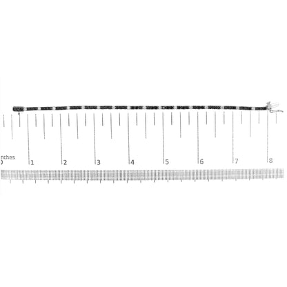 White metal bracelet with alternating round black and white gemstones in 4-prong settings, displayed horizontally on a ruler for size reference, shot from above.