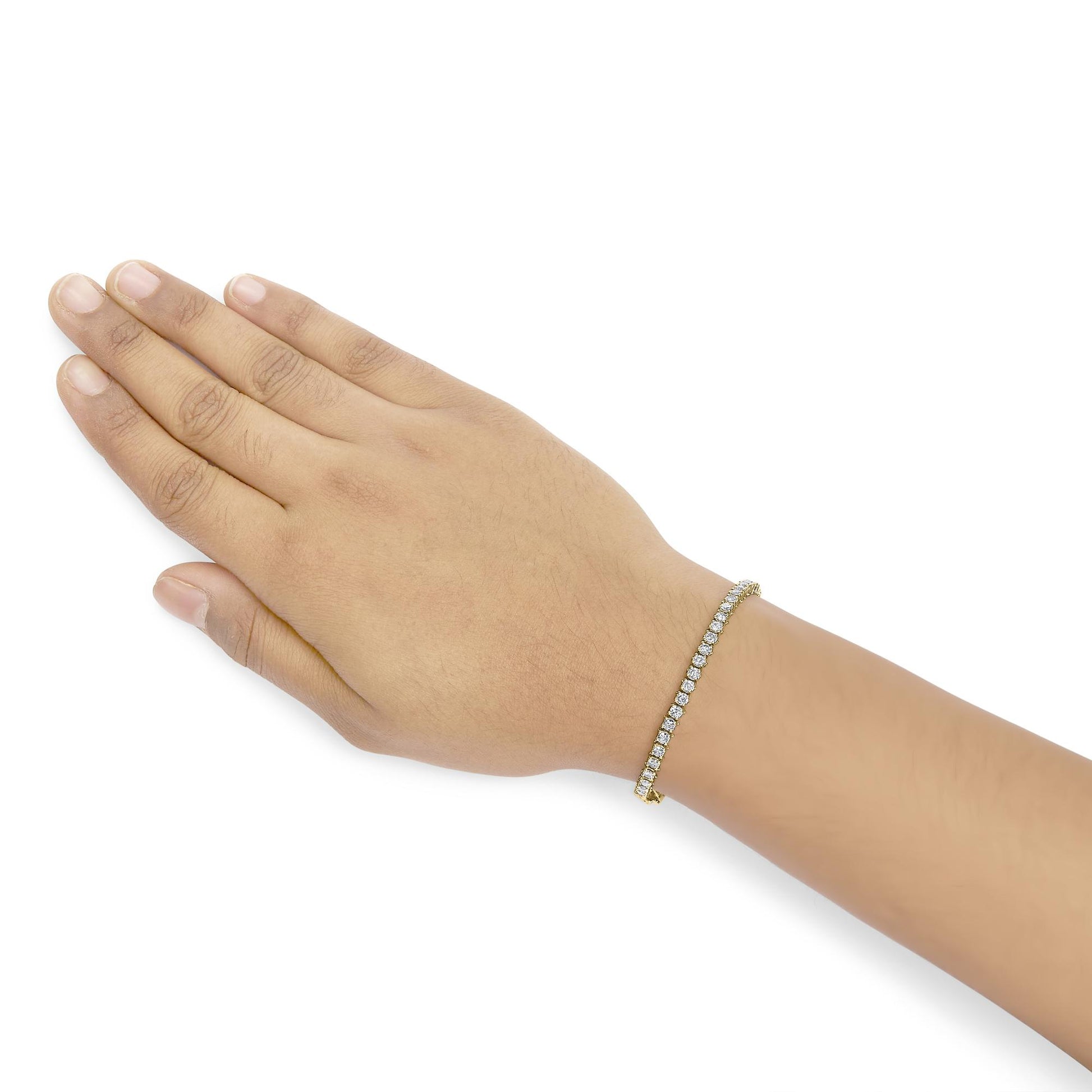 Yellow metal bracelet with white round gemstones in prong setting, shown on a model's wrist, angled top-down view.