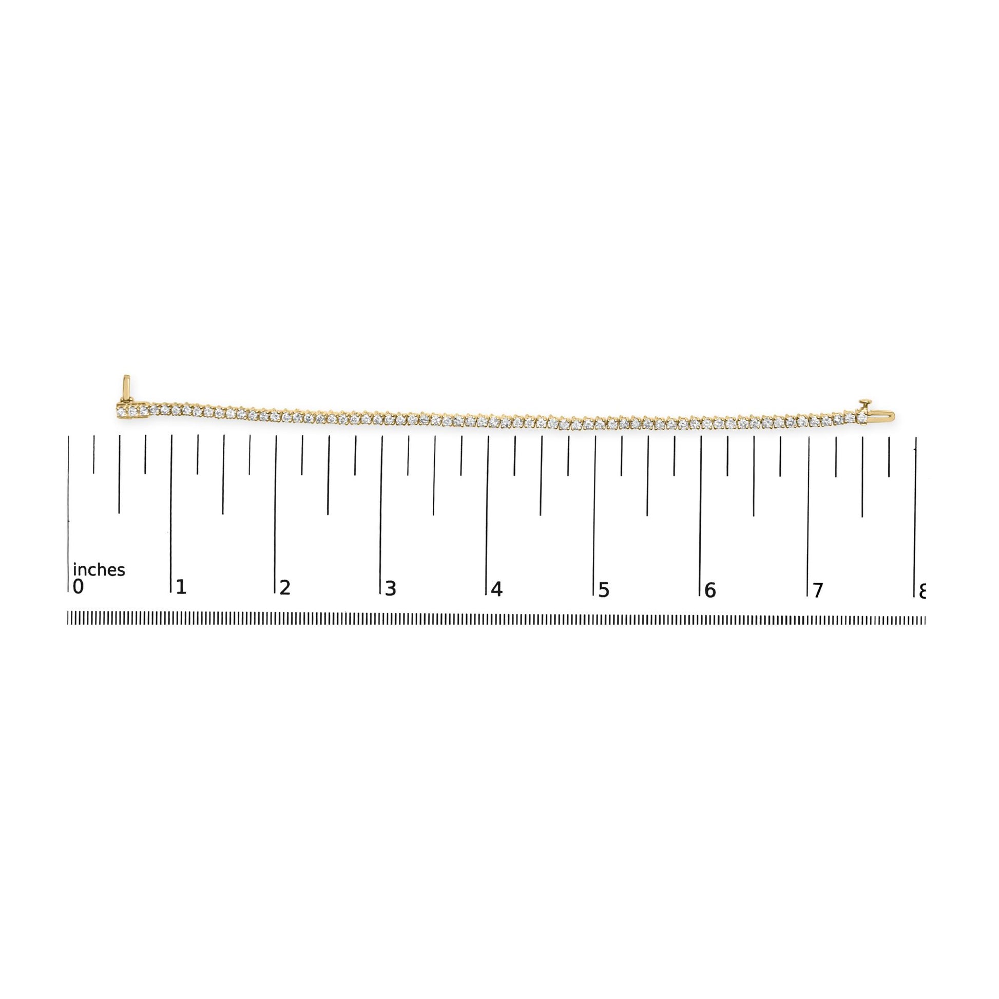 Yellow metal bracelet with prong-set round white gemstones, laid flat on ruler for size reference, top-down angle.