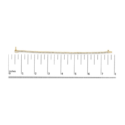 Yellow metal bracelet with prong-set round white gemstones, laid flat on ruler for size reference, top-down angle.