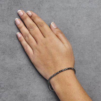 White metal bracelet with round black gemstones in prong settings, worn on a model's wrist, shown from a top angled view.