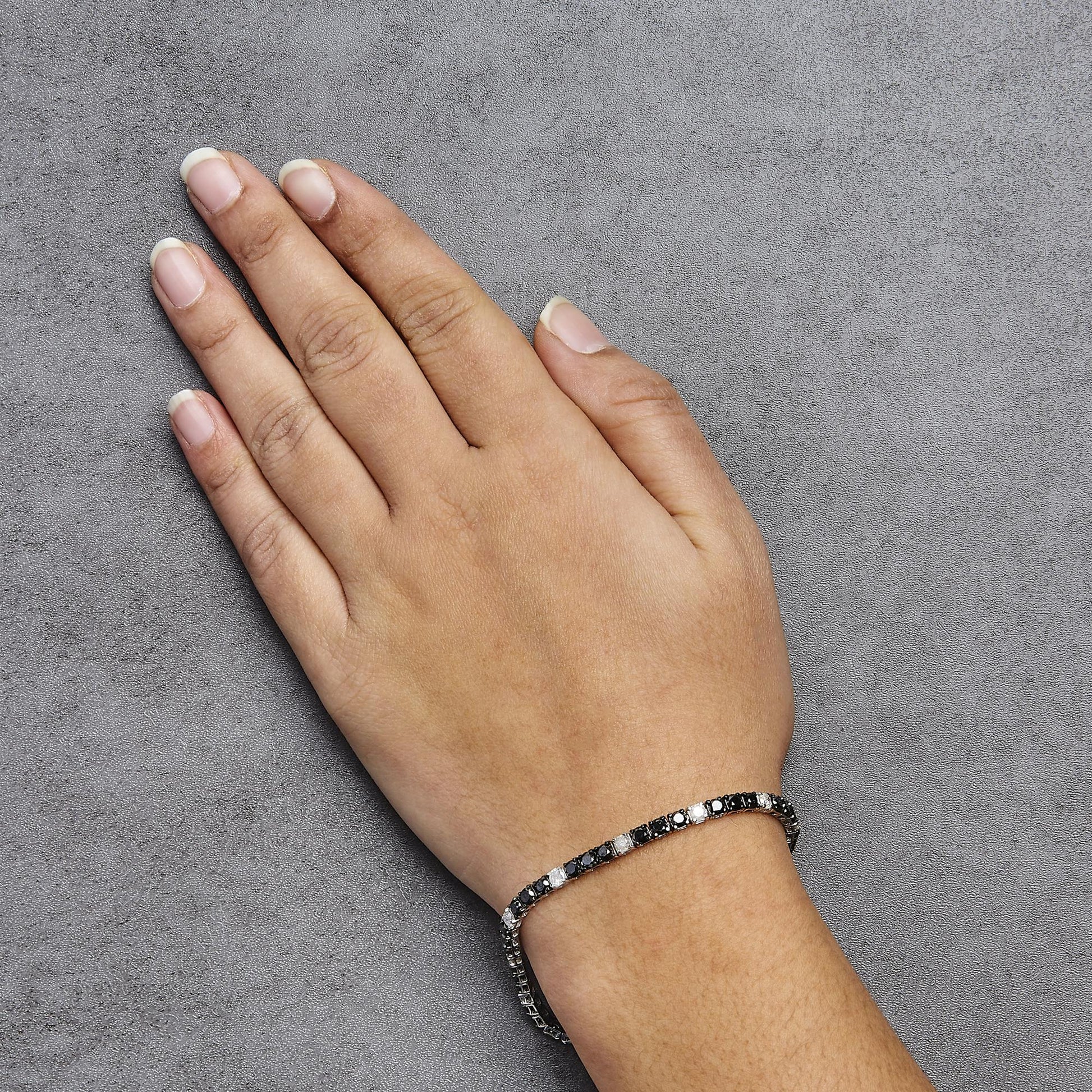 White metal bracelet with alternating black and white round gemstones in prong settings, worn on wrist, top-down angle.