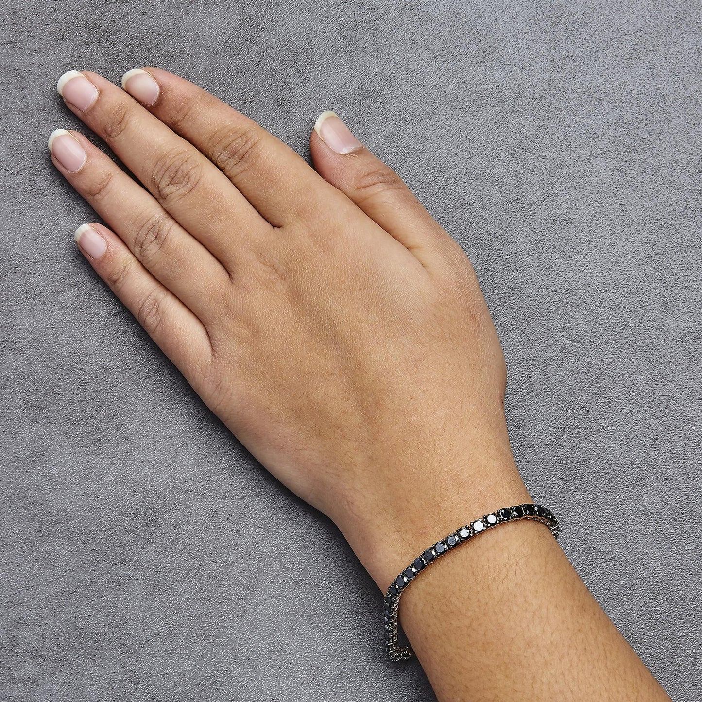 White metal bracelet with round black gemstones in prong settings, shown on a model's wrist from a top angle.
